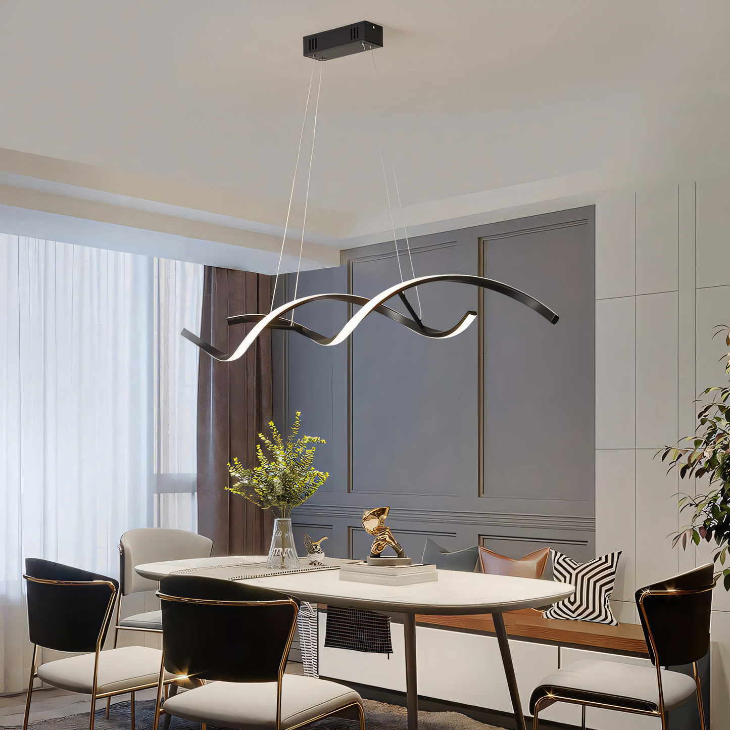 A gold, modern chandelier with swirling arms and clear crystals hangs from a dining room ceiling. The chandelier casts a warm, inviting glow on the space.