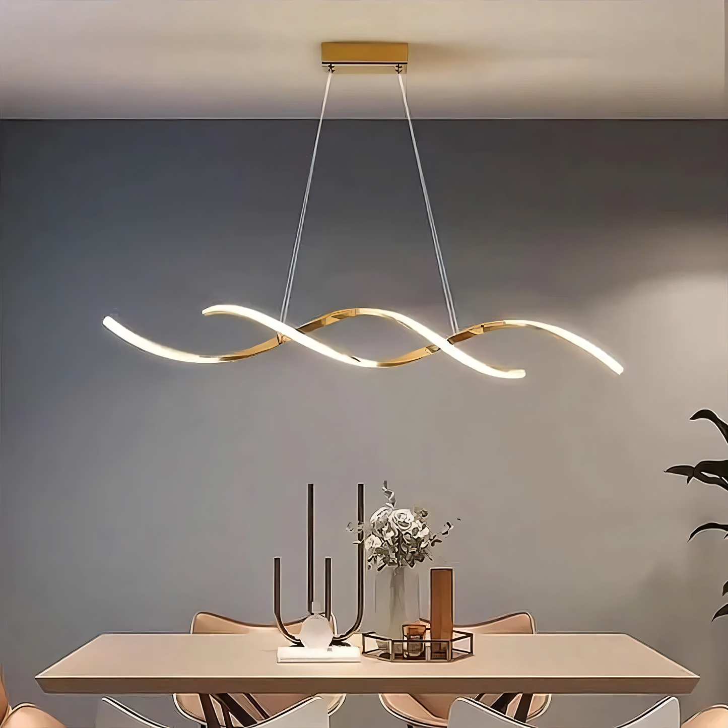 A gold, modern chandelier with swirling arms and clear crystals hangs from a dining room ceiling. The chandelier casts a warm, inviting glow on the space.