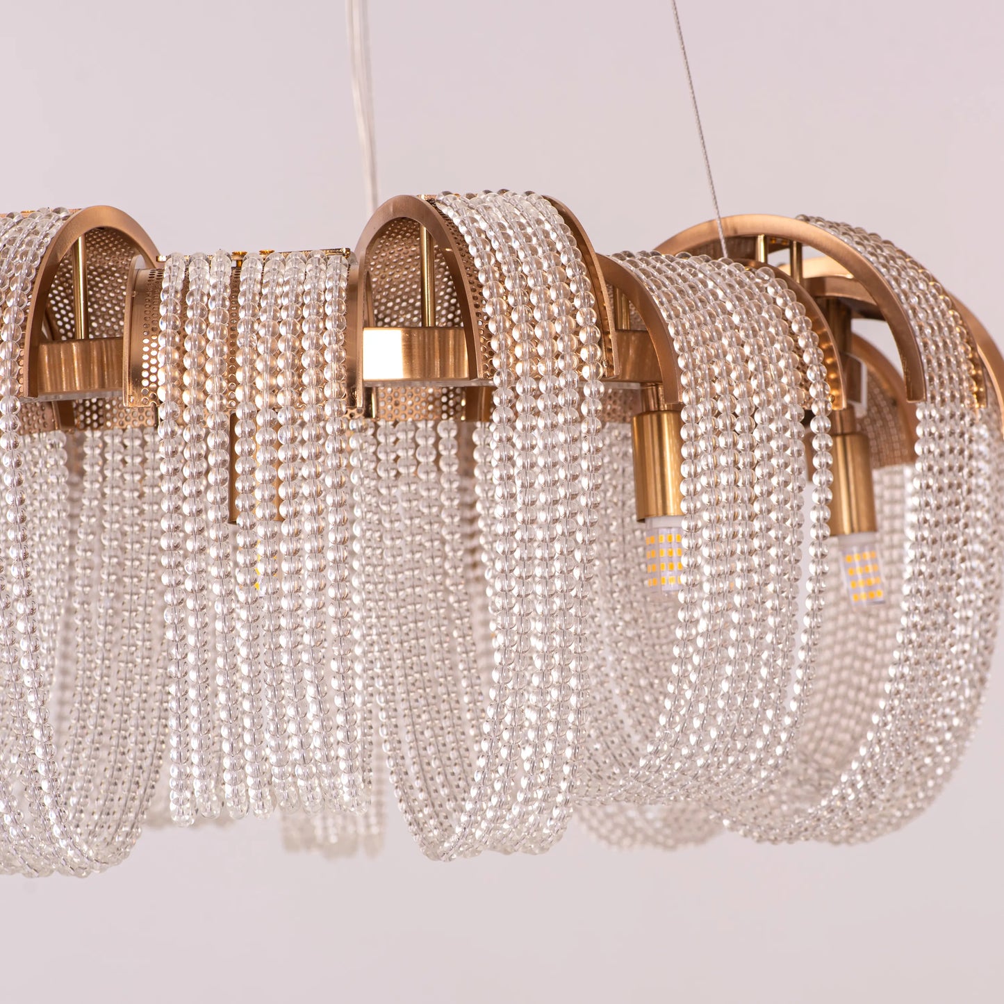 Medium-sized "Waves For Days" gold crystal chandelier with cascading tiers, illuminated and hanging in an elegant room.