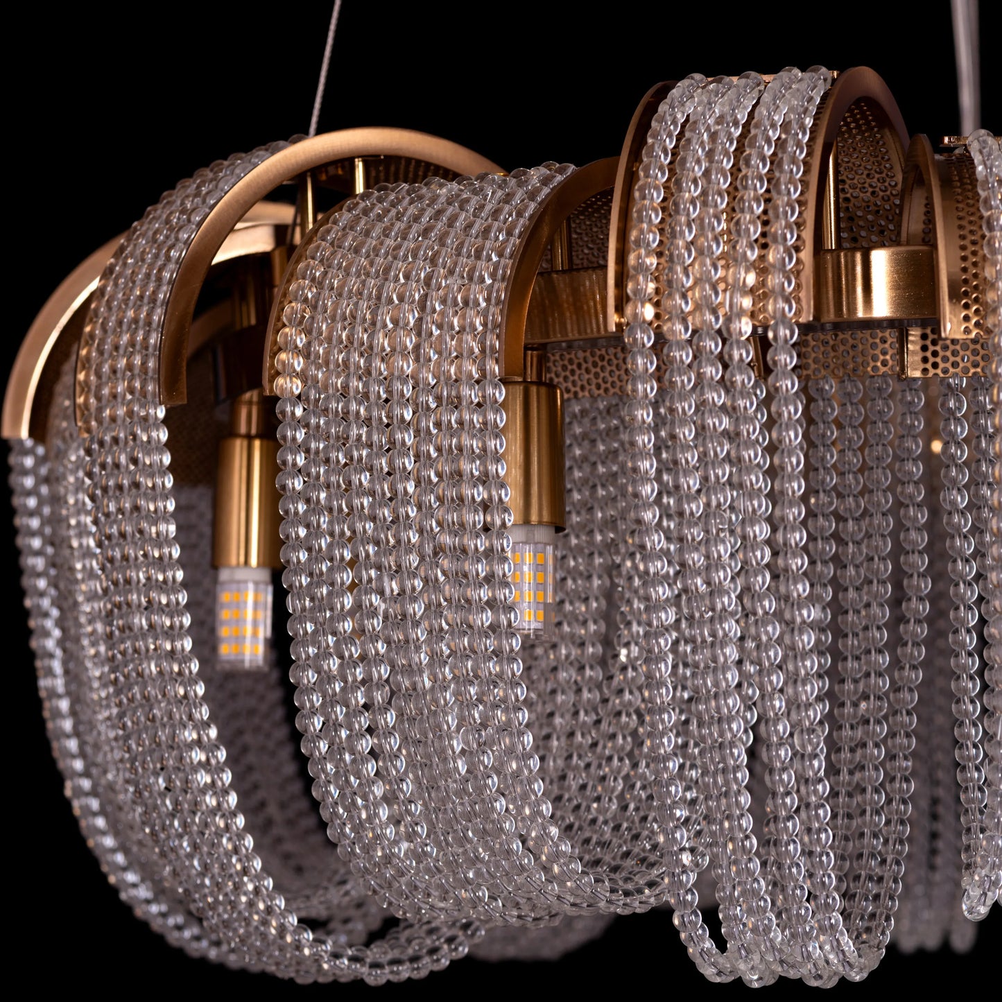 Medium-sized "Waves For Days" gold crystal chandelier with cascading tiers, illuminated and hanging in an elegant room.