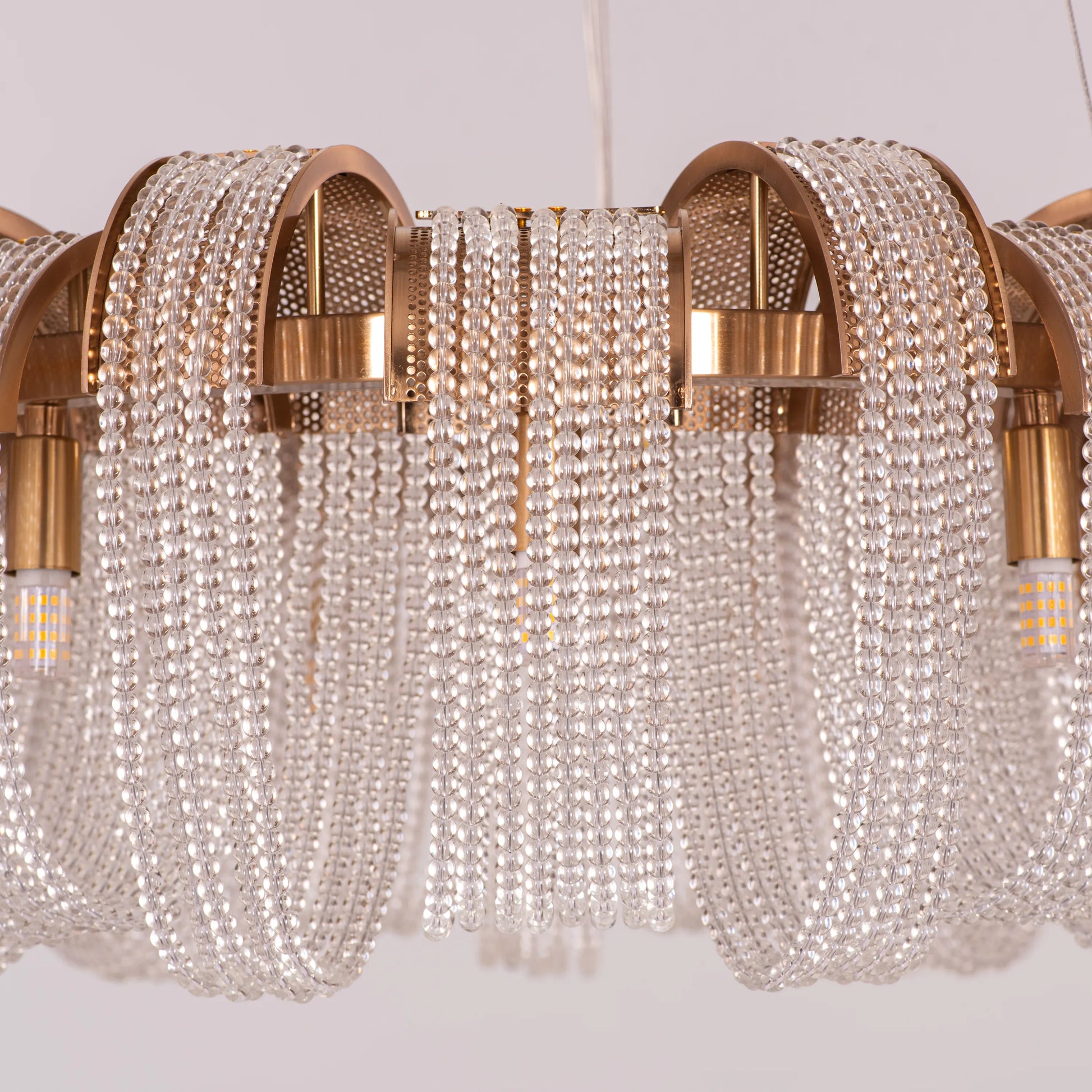 Medium-sized "Waves For Days" gold crystal chandelier with cascading tiers, illuminated and hanging in an elegant room.