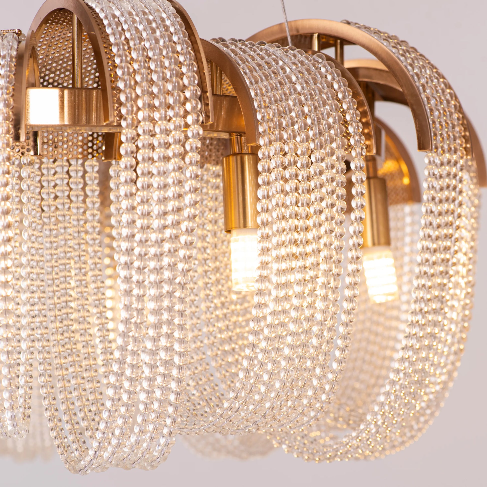 Medium-sized "Waves For Days" gold crystal chandelier with cascading tiers, illuminated and hanging in an elegant room.